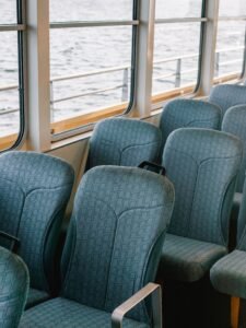 A serene view of unoccupied blue seats inside a boat with windows showing the sea.