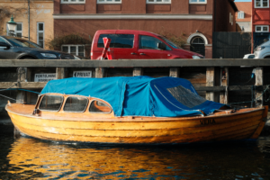 Wooden boat with blue cover docked in a canal next to urban architecture.