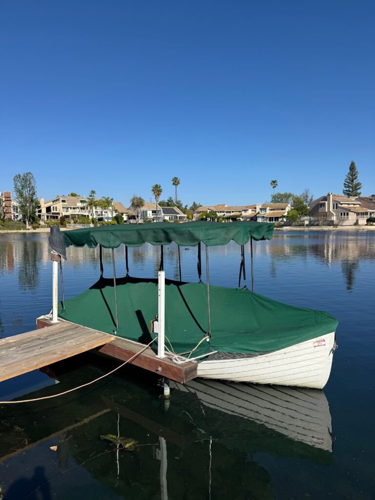 pexels photo 36503234 36503234 A tranquil scene of a covered boat docked on a lake with residential houses in the background.